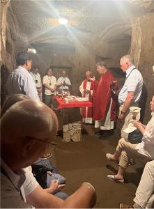 People gathered in a dark room carved out of stone, with priests holding a service