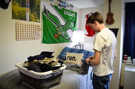A student folds laundry on their bed - there is a pillow that says run, and an Eagles poster