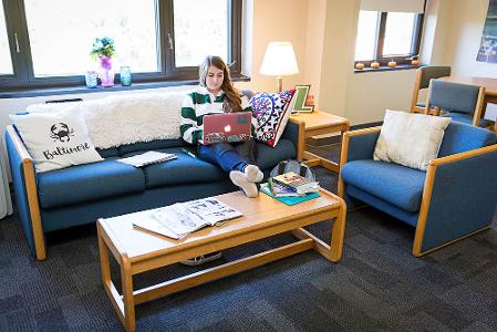 A student in a decorated dorm lounge with a laptop and her feet on the coffee table