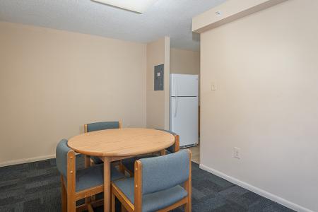 Table with three chairs with a fridge in the background in a different room