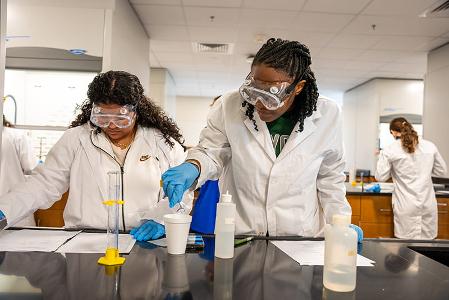 Students conducting lab work with safety goggles and gloves on.