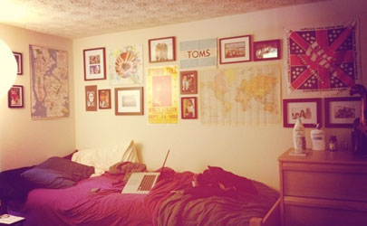 A dorm room with a grid of posters and frames on the wall and a laptop on the bed