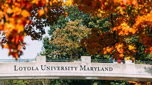 Orange fall foliage surrounds a bridge with the words Loyola University Maryland