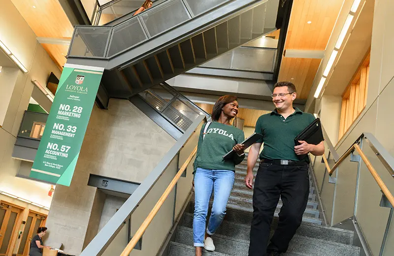 A professor and student walk down the stairs of the Sellinger building
