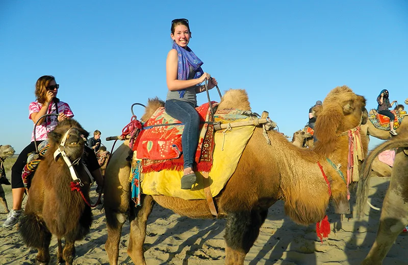 Student sitting and smiling on a camel in a desert