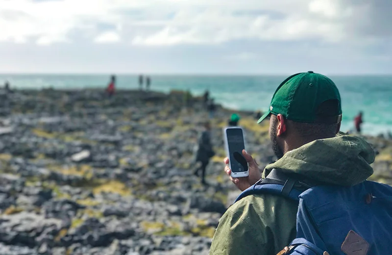 A student takes a photo with his cell phone on a rocky cliff overlooking the ocean