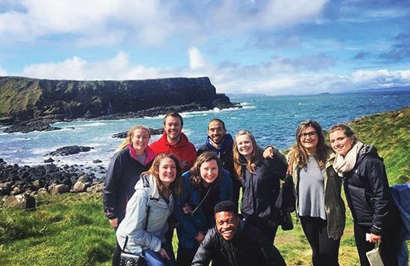 Students smiling for the camera on a grassy field overlooking the ocean