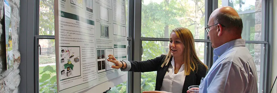 A student talking to someone about her poster during a research symposium