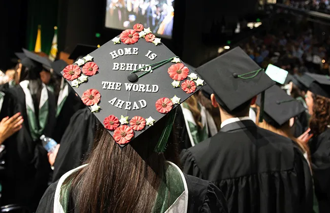 Close-up of a commencement cap, with text that reads: Home is behind, the world ahead